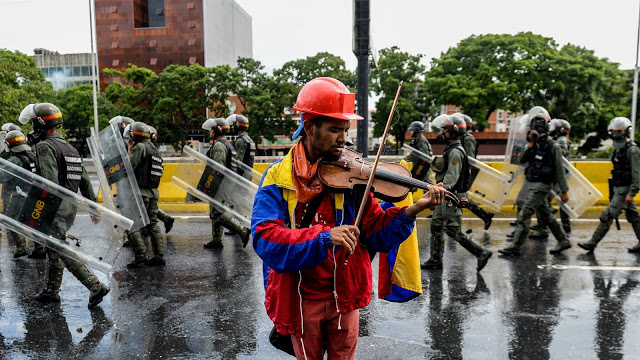 Một người biểu tình chơi đàn, trong khi binh lính được Chính phủ Venezuela điều đi để trấn áp. Ảnh: FEDERICO PARRA/AFP/Getty Images