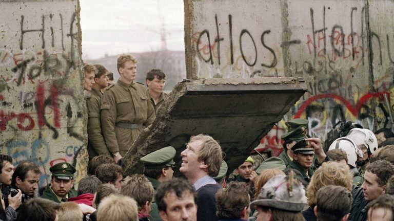 Lính biên phòng Đông Đức nhìn những người biểu tình kéo sập một đoạn của Bức tường Berlin gần Cổng Brandenburg vào tháng 11 năm 1989. Ảnh: Lionel Cironneau/AP