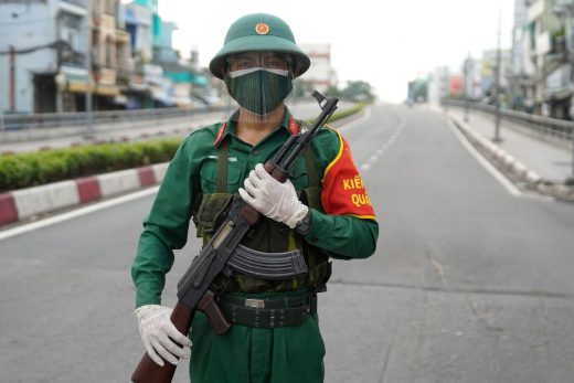 Một lính bộ đội cầm súng AK đứng canh gác trên một con đường vắng bóng người ở Sài Gòn hôm 23/8/2021, sau khi chính quyền thành phố áp dụng lệnh phong tỏa đến ngày 16/9 để ngăn dịch Covid-19. Ảnh: Pham Tho/AFP via Getty Images
