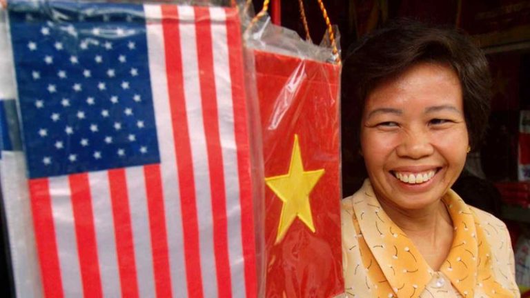 Một người đứng cạnh cờ Mỹ và Việt Nam bày bán ở quầy hàng của mình ở Hà Nội. Ảnh: Reuters