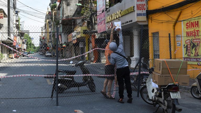 Một người dân nhận hàng từ shipper qua hàng rào trong khu vực cách ly ở Hà Nội ngày 6/9/2021. Ảnh: Reuters