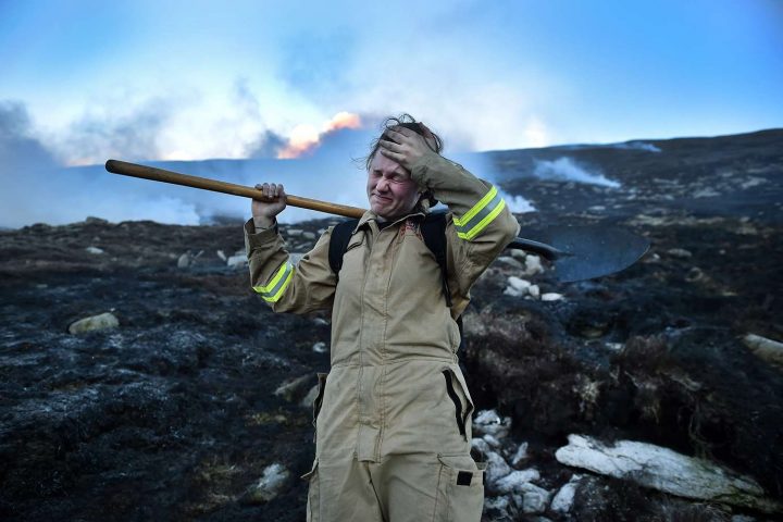 Cô Haley Agnew đang lau mồ hôi trán khi cùng với nhiều nhân viên cứu hỏa khác chiến đấu chống lại đám cháy khủng khiếp trên sườn núi Slieve Donard ở Newcastle, Bắc Ireland, vào ngày 24/4/2021. Ảnh: CHARLES MCQUILLAN/GETTY IMAGES