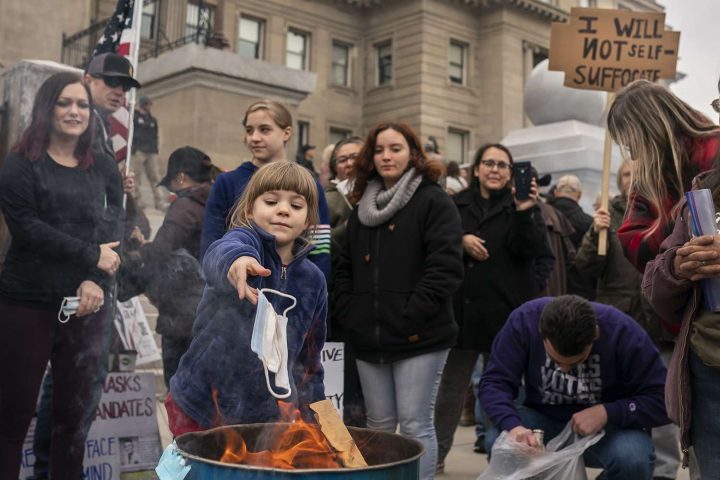 Một đứa trẻ ném khẩu trang vào lửa trong một cuộc biểu tình trước trụ sở Hạ Viện Tiểu Bang Idaho ở thủ phủ Boise hôm 6/3/2021. Người dân và các chính trị gia, bao gồm Trung Tướng Janice McGeachin, đã tụ tập tại ít nhất 20 thành phố trên toàn tiểu bang để phản đối những hạn chế (tự do cá nhân) nhằm giảm thiểu lây nhiễm COVID-19 của chính quyền. Ảnh: NATHAN HOWARD/ GETTY IMAGES