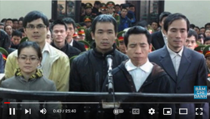 TNLT Hồ Đức Hòa (bìa phải) tại phiên tòa sơ thẩm ở Nghệ An hôm 9/1/2013 cùng 13 người khác. Ông bị tuyên án 13 năm tù giam với cáo buộc “hoạt động nhằm lật đổ chính quyền nhân dân” theo điều 79, BLHS (cũ, nay là điều 109). Ảnh chụp từ Youtube Việt Tân