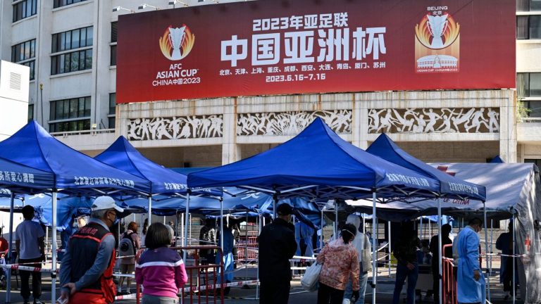 Nền kinh tế Trung Quốc chậm lại là do chính sách chống dịch cứng ngắc “zero-Covid.” Trong hình, người dân Trung Quốc xét nghiệm Covid-19 tại một tòa nhà có bảng quảng cáo về Asian Cup 2023 ở Bắc Kinh. Trung Quốc đã rút khỏi tư cách chủ nhà Asian Cup 2023 do virus Corona. Ảnh: Jade Gao/AFP via Getty Images