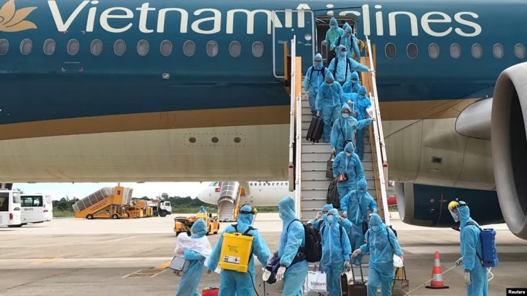 Nhân viên y tế xịt thuốc trừ khuẩn những công dân Việt Nam hồi hương sau khi đáp chuyến bay do Bộ Ngoại giao tổ chức từ Singapore xuống sân bay Cần Thơ trong thời gian đại dịch Covid-19 hôm 7/8/2020. Ảnh: Reuters