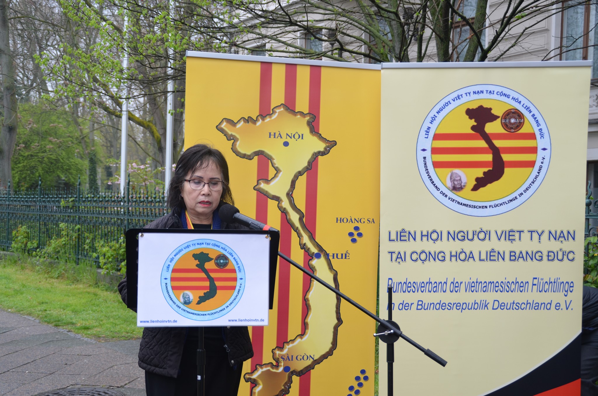 Bác sĩ Hoàng Thị Mỹ Lâm, Chủ tịch Liên Hội Ngưòi Việt Tỵ Nạn tại CHLB Đức mở đầu ngày sinh hoạt đấu tranh 30/4 bằng diễn văn khai mạc cuộc biểu tình trước Đại sứ quán CSVN tại Berlin (tòa nhà phía sau)
