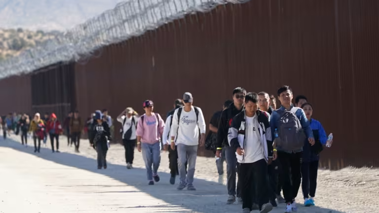 Một nhóm người, trong đó có nhiều người đến từ Trung Quốc, đi dọc bức tường biên giới sau khi vượt biên giới từ Mexico vào Mỹ để xin tị nạn gần Jacumba, California, vào ngày 24/10/2023. Ảnh: AP